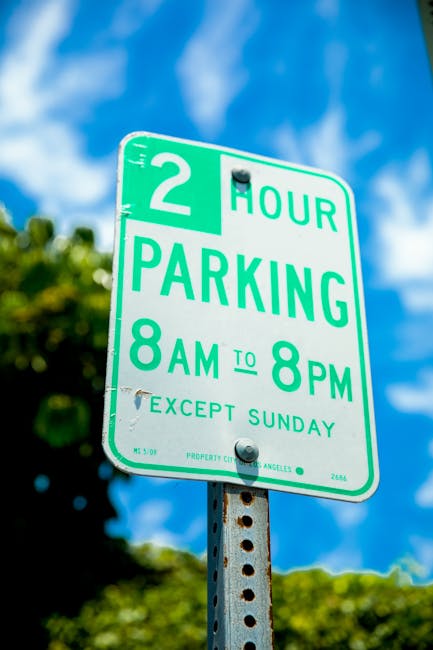 A close-up photograph of a green and white parking restriction sign mounted on a metal pole, displaying a 2-hour parking limit from 8 am to 8 pm, with a note indicating the restriction does not apply